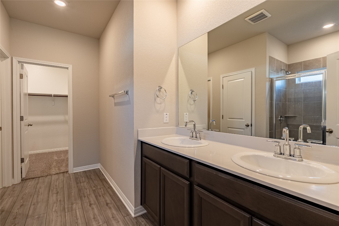 107 Cona Way Hutto, TX 78634 - Photo 14 of 26 Bathroom featuring double vanity, light wood-type flooring, a shower stall, recessed lighting, and a spacious closet