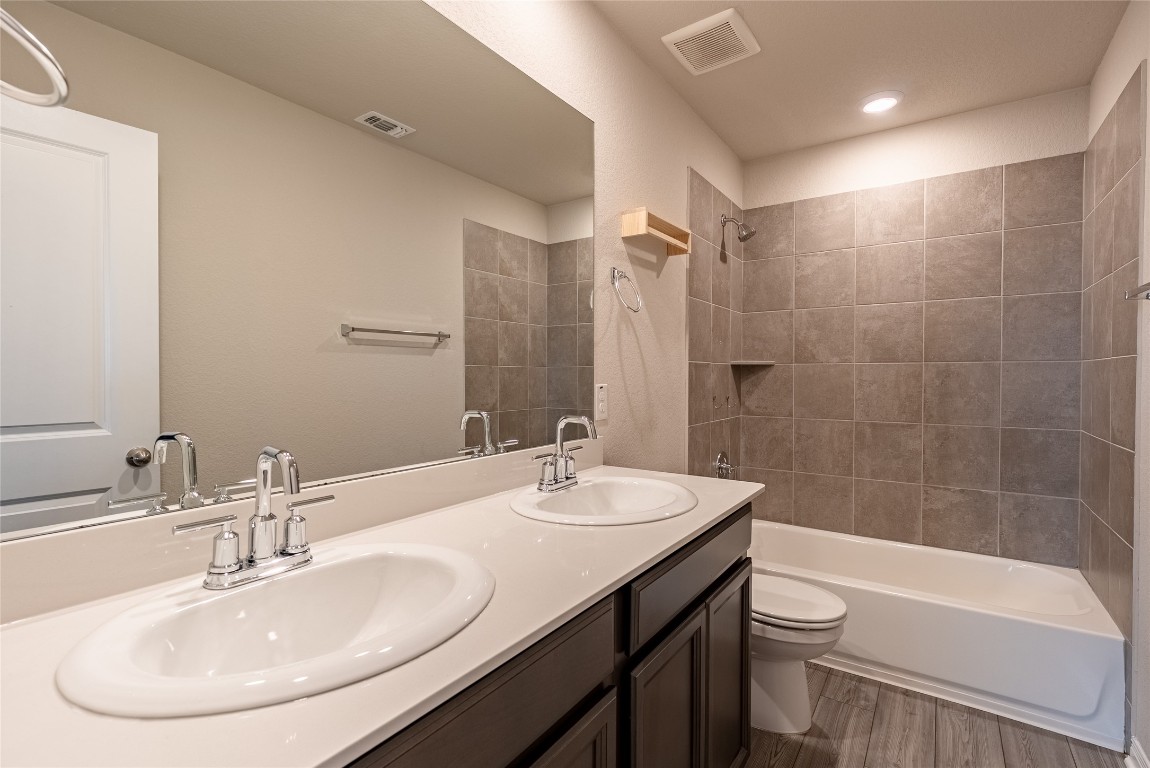 107 Cona Way Hutto, TX 78634 - Photo 24 of 26 Bathroom with light wood-style floors, double vanity, and shower / washtub combination