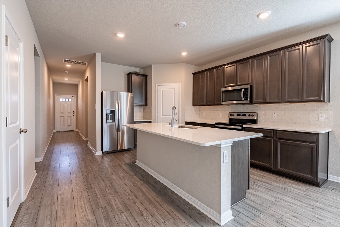 107 Cona Way Hutto, TX 78634 - Photo 3 of 26 Kitchen featuring backsplash, appliances with stainless steel finishes, dark brown cabinetry, recessed lighting, and light wood finished floors