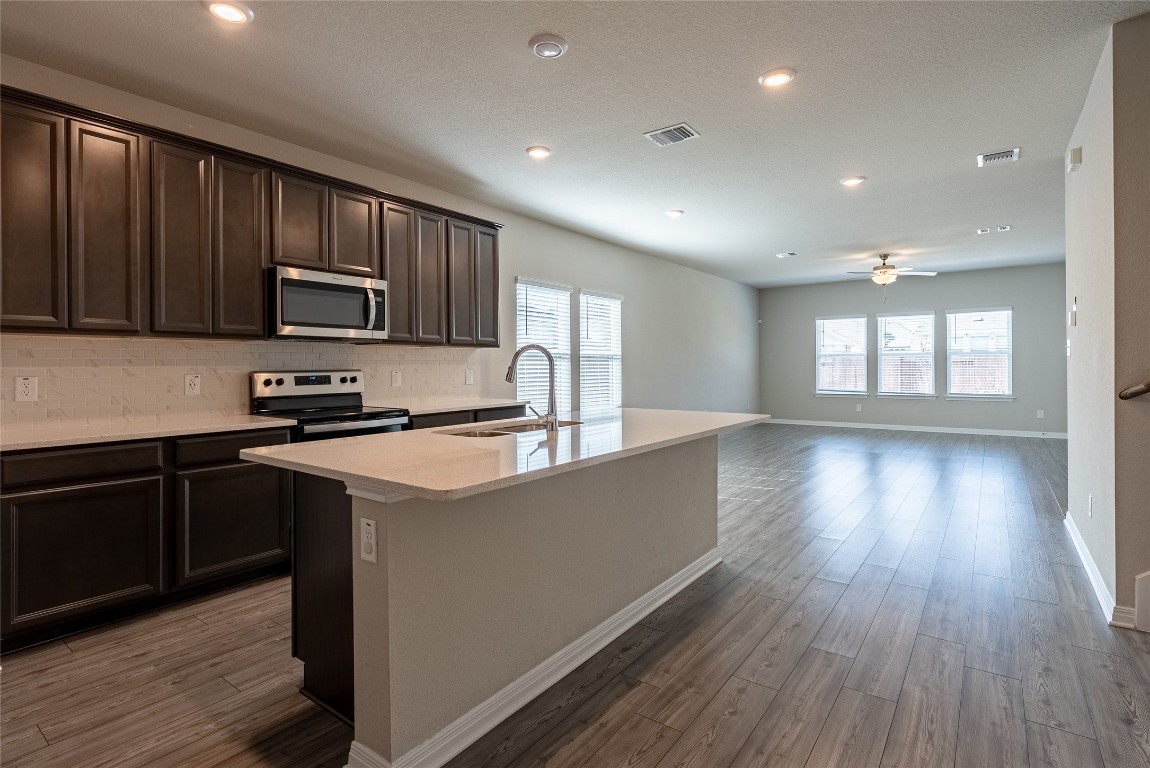 107 Cona Way Hutto, TX 78634 - Photo 4 of 26 Kitchen featuring decorative backsplash, dark brown cabinetry, appliances with stainless steel finishes, a center island with sink, and light stone counters