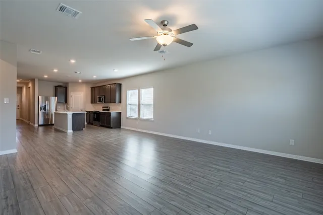 a view of an empty room with wooden floor and a kitchen