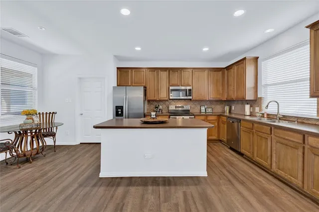 a kitchen with stainless steel appliances granite countertop wooden cabinets a sink a stove a dining table and chairs