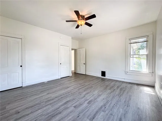 an empty room with wooden floor chandelier fan and windows