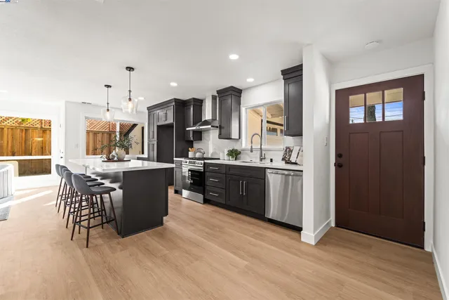 a kitchen with stainless steel appliances kitchen island granite countertop a stove a sink a refrigerator and a dining table with wooden floor