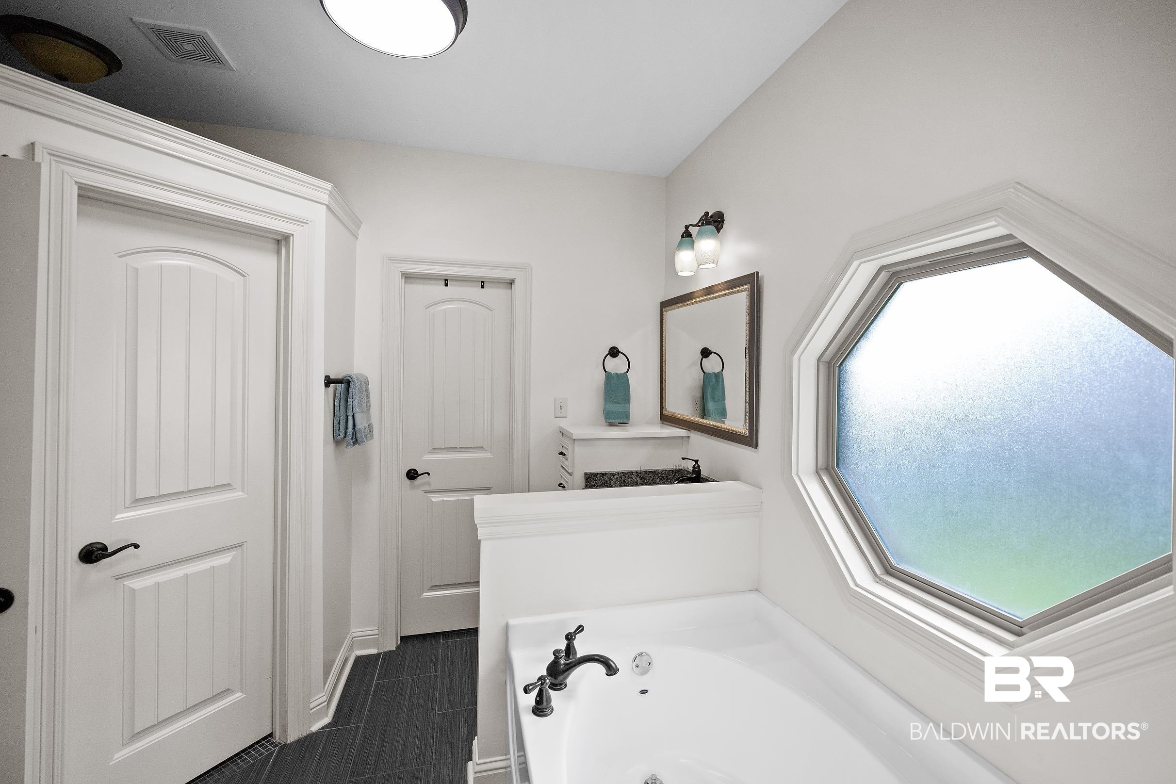 313 Pecan Ridge Boulevard Fairhope, AL 36532 - Photo 44 of 51 Bathroom featuring an octagon window with frosted glass, a built-in tub with dark bronze fixtures, dark tile flooring, and two white panel doors