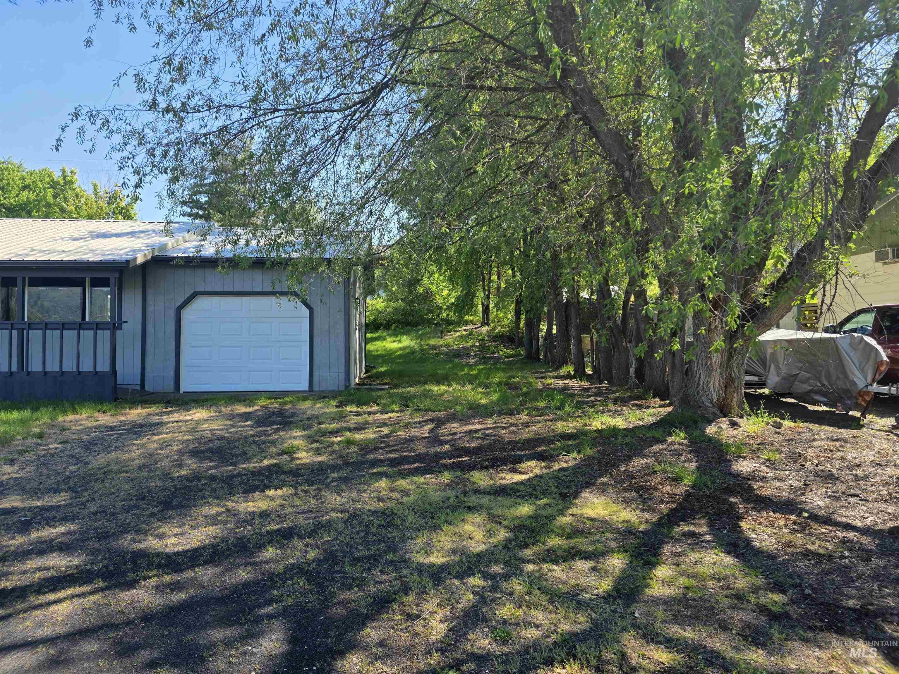310 Fir Road Kamiah, ID 83536 - Photo 29 of 32 Exterior featuring an attached garage with a white panel door, a covered porch with dark railings, and a gravel driveway