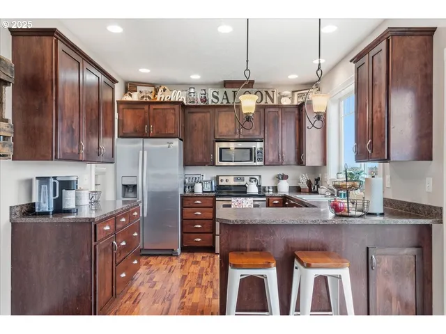 a kitchen with stainless steel appliances granite countertop a refrigerator a sink dishwasher a stove with wooden cabinets and floor