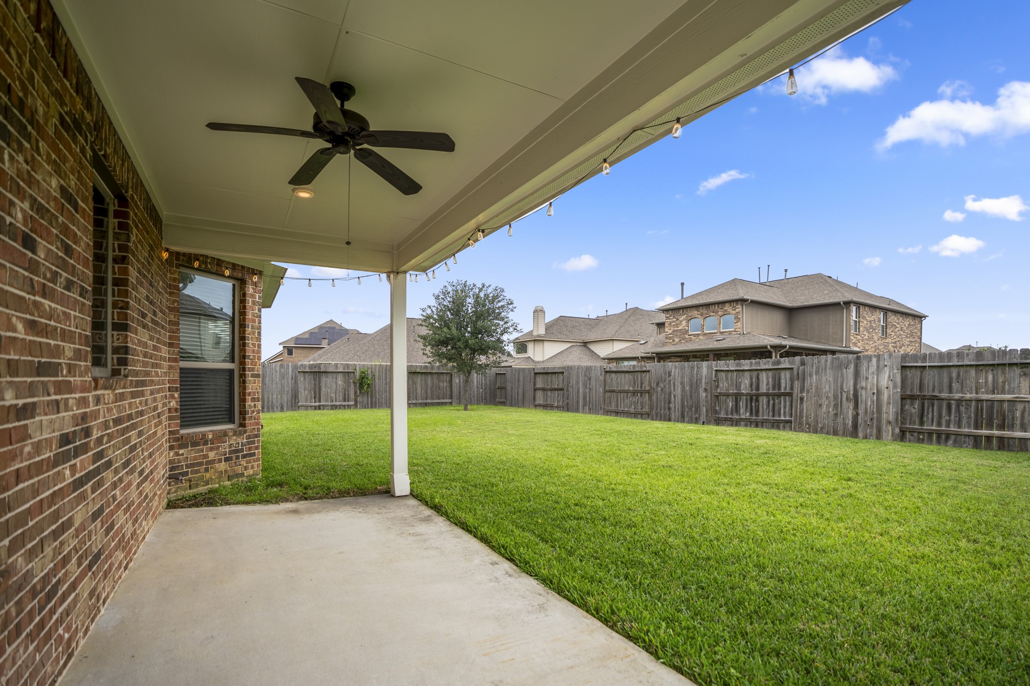 7502 Windsor Park Court Spring, TX 77379 - Photo 40 of 50 Stepping outside, the covered patio extends the main living spaces into the backyard, complete with a ceiling fan, string lights, and a convenient external gas connection—making it easy to add a grill or outdoor kitchen setup and enjoy evenings outside with plenty of shade already in place.