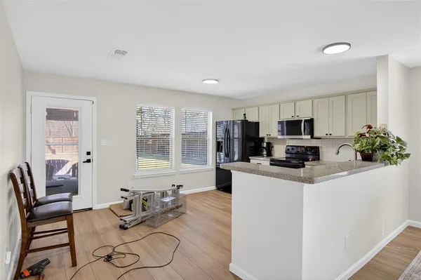 a kitchen with stainless steel appliances kitchen island granite countertop a refrigerator a stove a sink a dining table and chairs with wooden floor