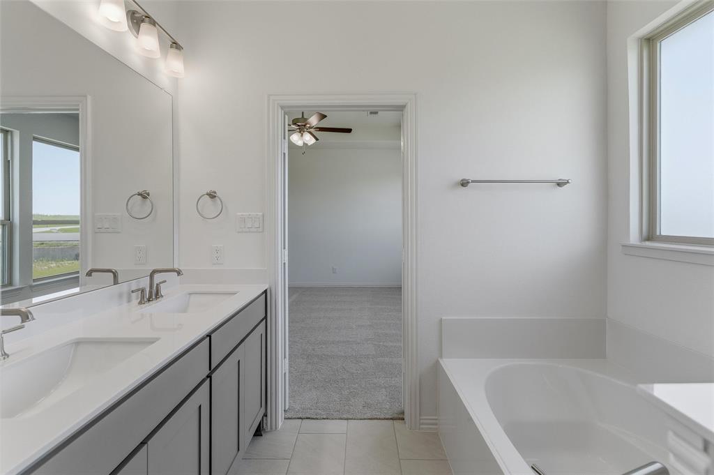 130 Fossil Canyon Drive Rhome, TX 76078 - Photo 19 of 25 Bathroom featuring a dual vanity with undermount sinks, a large mirror with overhead lighting, a built-in bathtub, and a window with frosted glass