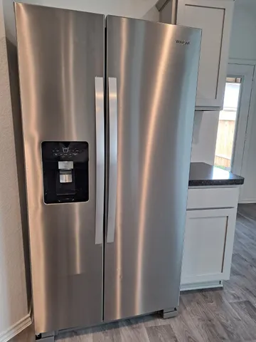 a view of a refrigerator in kitchen and an empty room with wooden floor