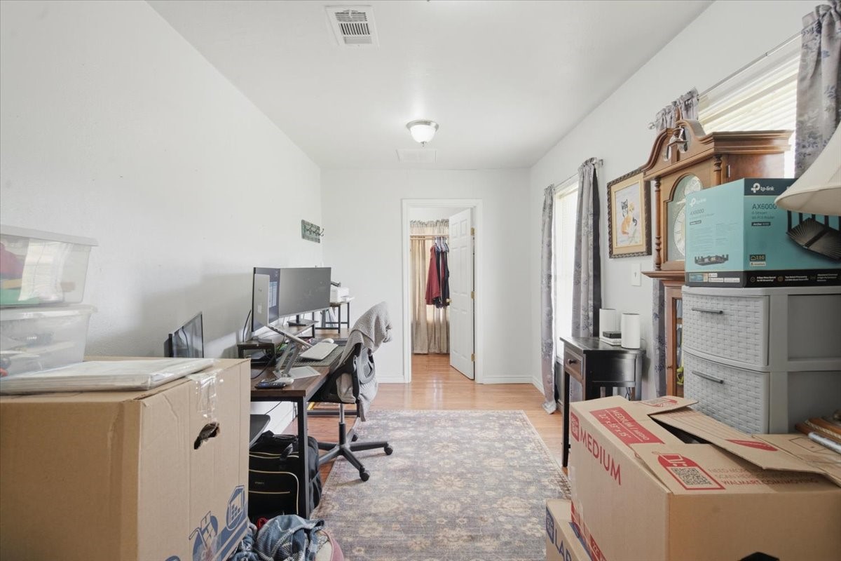 765 Norcross Road Wallis, TX 77485 - Photo 15 of 42 This photo shows a bright, narrow room with wood floors, currently used as an office space. Natural light enters through two windows with curtains. The space has a simple, functional layout, ideal for a home office or study.