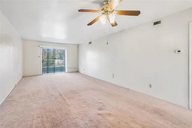 an empty room with chandelier fan and windows