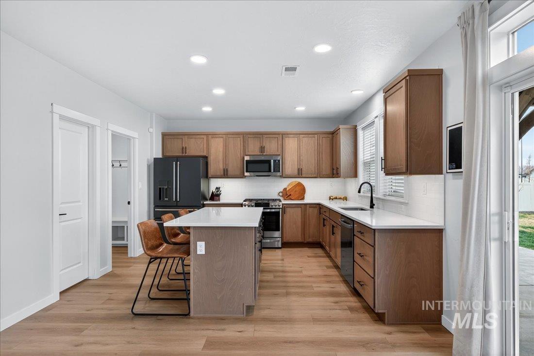 1993 North Perth Court Middleton, ID 83644 - Photo 18 of 45 Kitchen with stainless steel appliances, a kitchen island, a breakfast bar area, light wood finished floors, and decorative backsplash