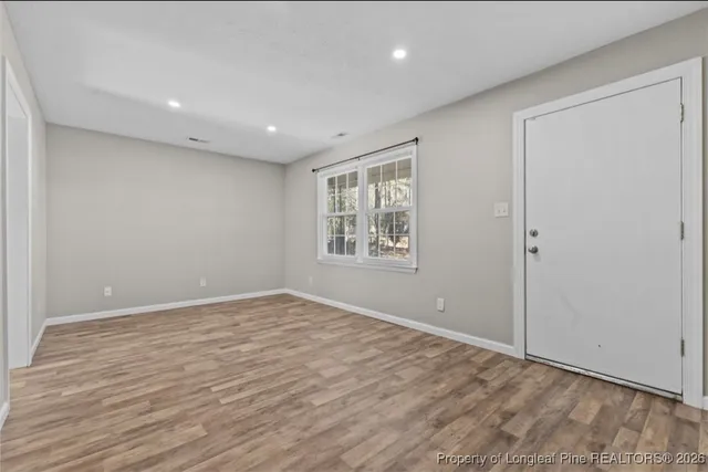 a view of an empty room with wooden floor and a window