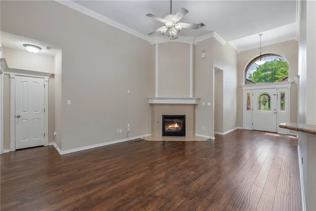 an empty room with wooden floor a ceiling fan a fireplace and windows