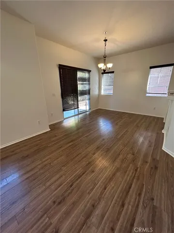 an empty room with wooden floor chandelier and windows