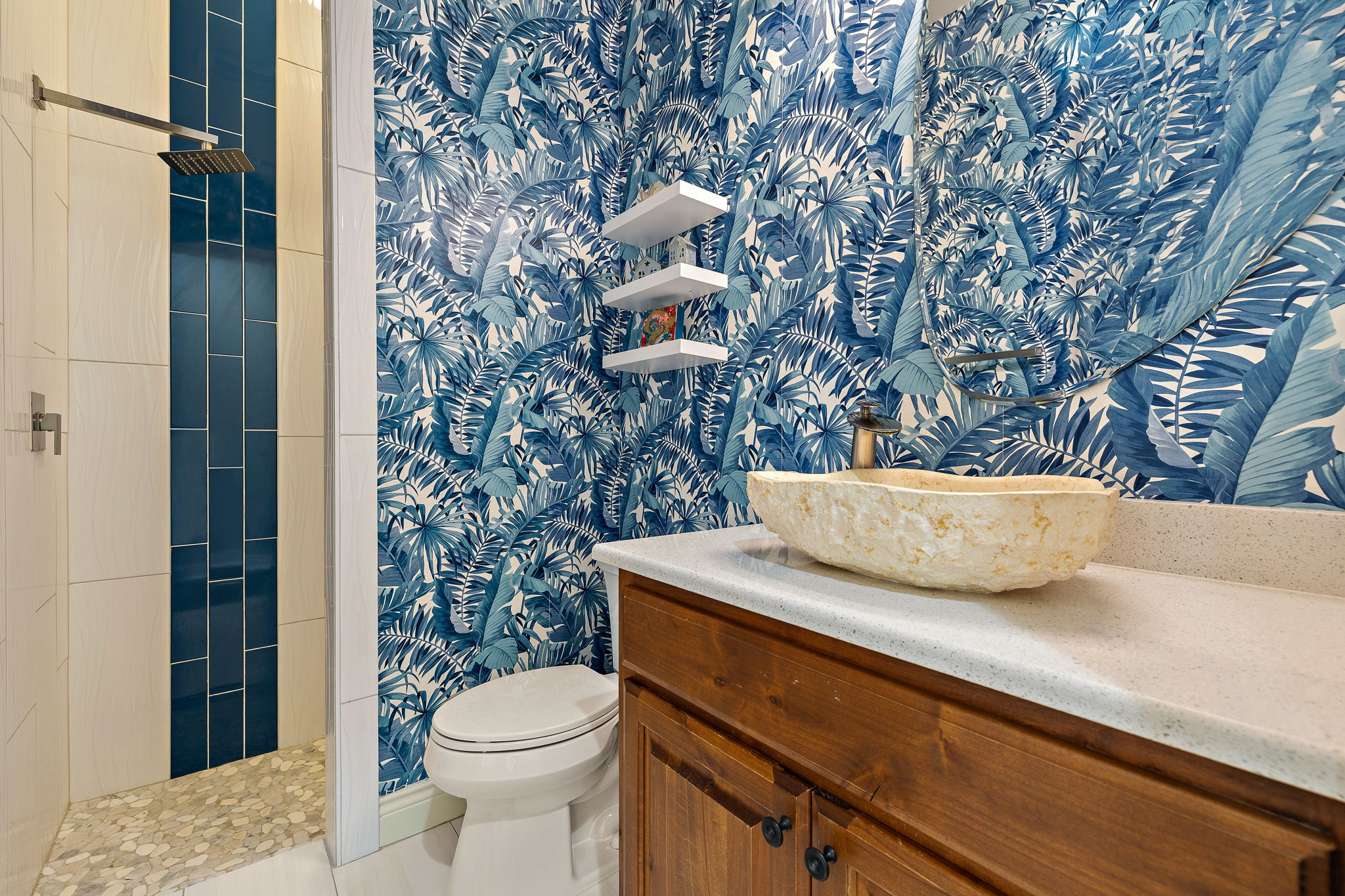 231 Marbella Way Georgetown, TX 78633 - Photo 28 of 40 Bold, tropical wallpaper envelops this well-appointed bathroom, featuring a stone vessel sink and a tiled shower with a rain-style showerhead.