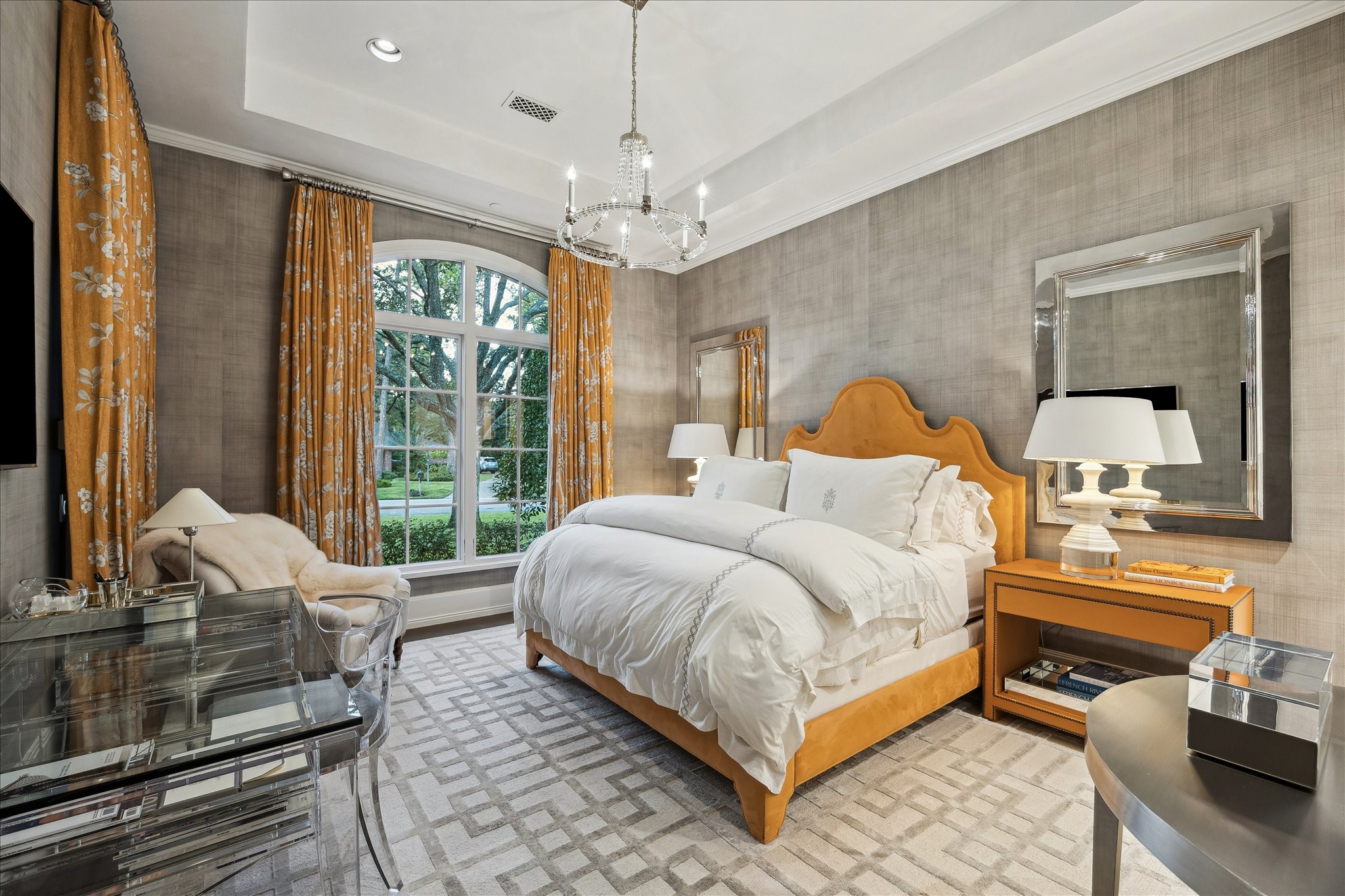 220 Merrie Way Lane Houston, TX 77024 - Photo 28 of 50 Designer wallpaper, wide-plank oak flooring, and a tray ceiling with recessed lighting and a crystal chandelier elevate this downstairs bedroom. An arched window brings in natural light, while a built-in coffee bar with marble finishes and a beverage refrigerator completes the room.