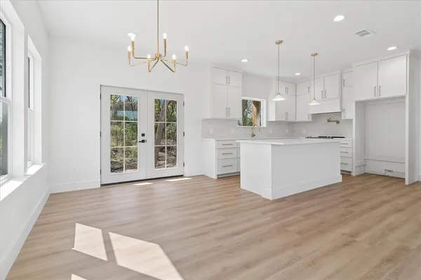 a large white kitchen with kitchen island a stove a sink dishwasher and white cabinets with wooden floor