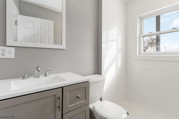 a bathroom with a toilet a sink a mirror a window and vanity