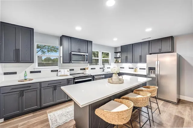 a kitchen with stainless steel appliances granite countertop a sink a stove a refrigerator cabinets and chairs