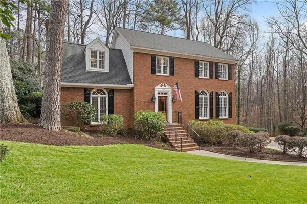 a view of a brick house with a yard plants and large tree
