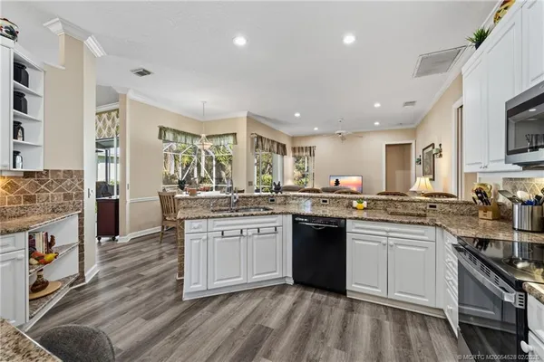 a kitchen with stainless steel appliances granite countertop a stove top oven a sink dishwasher and a refrigerator with wooden floor