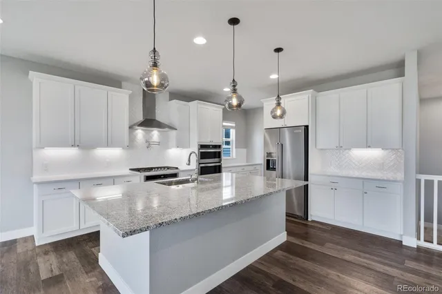 a large kitchen with granite countertop a stove a sink a center island a refrigerator and a wooden floor