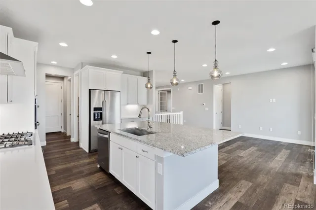a kitchen with stainless steel appliances kitchen island granite countertop a refrigerator a sink and a wooden floors