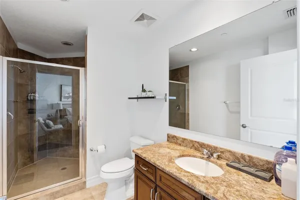 a bathroom with a granite countertop sink a toilet a mirror and shower