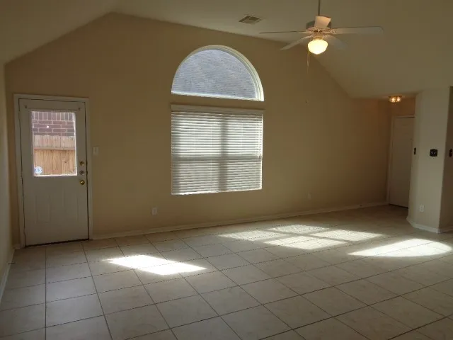a view of an empty room with window and chandelier fan