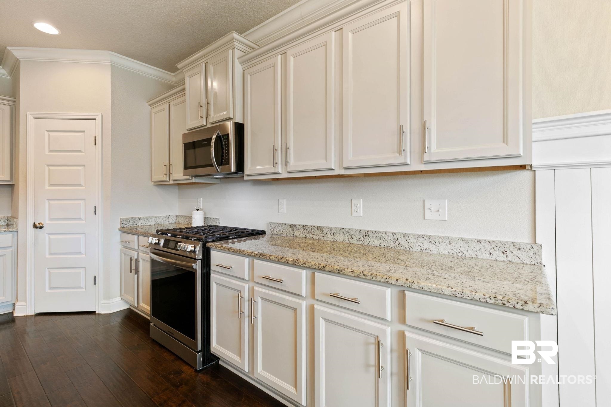 31187 Spoonbill Road Daphne, AL 36527 - Photo 18 of 85 Modern kitchen featuring white cabinetry, light granite countertops, a stainless steel range with gas cooktop, a stainless steel microwave, and dark wood-finish flooring