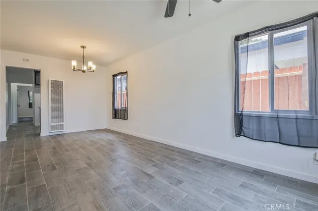 an empty room with chandelier fan and windows