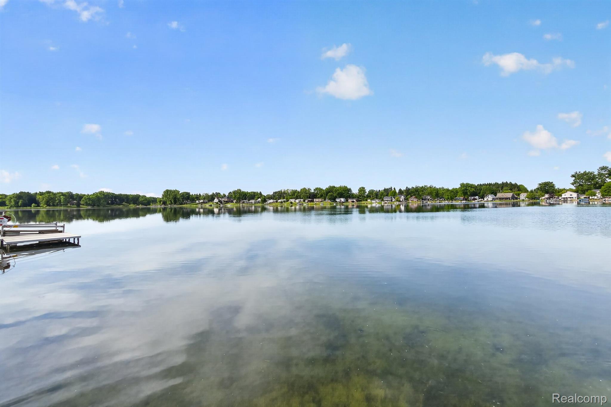 1717 Triangle Lake Road Howell, MI 48843 - Photo 21 of 58 Expansive waterfront setting featuring a tranquil lake, clear blue sky, and a wooden dock structure