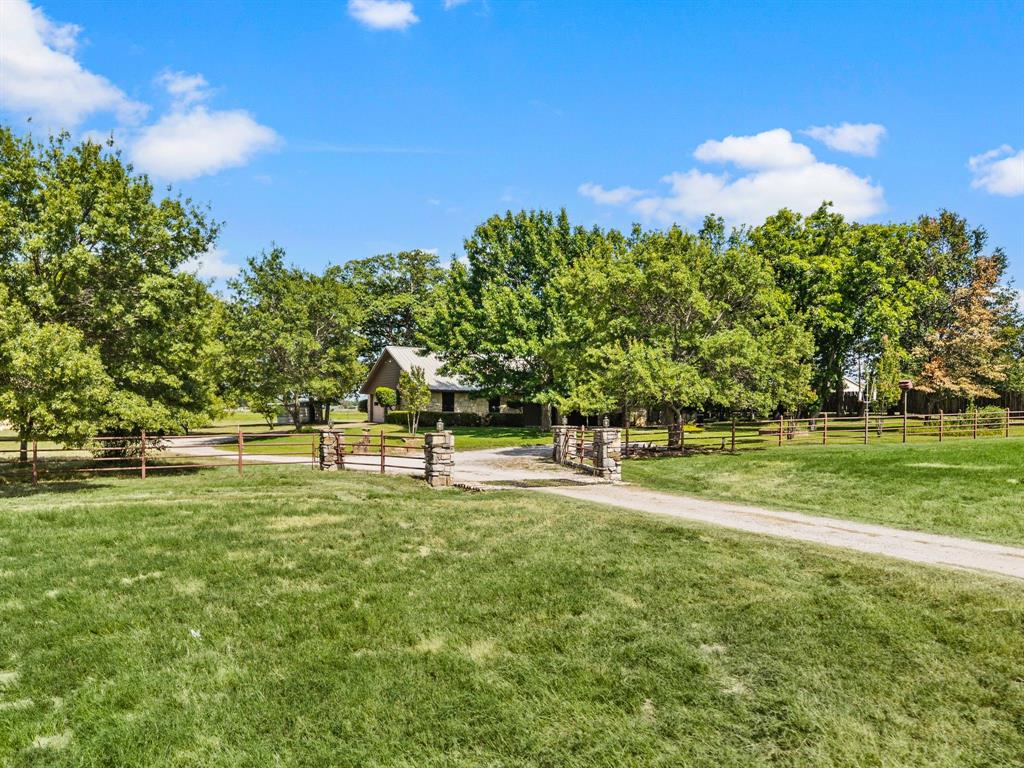 515 New Highland Road Springtown, TX 76082 - Photo 36 of 38 Gravel driveway entrance with stone pillars, surrounded by mature trees and expansive green lawn, leading to a visible residence with a pitched roof