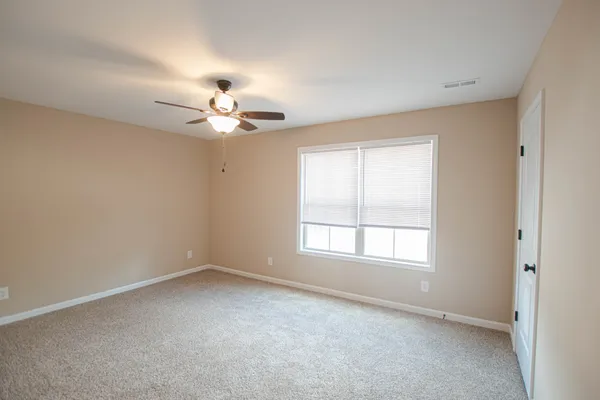 an empty room with chandelier fan and windows
