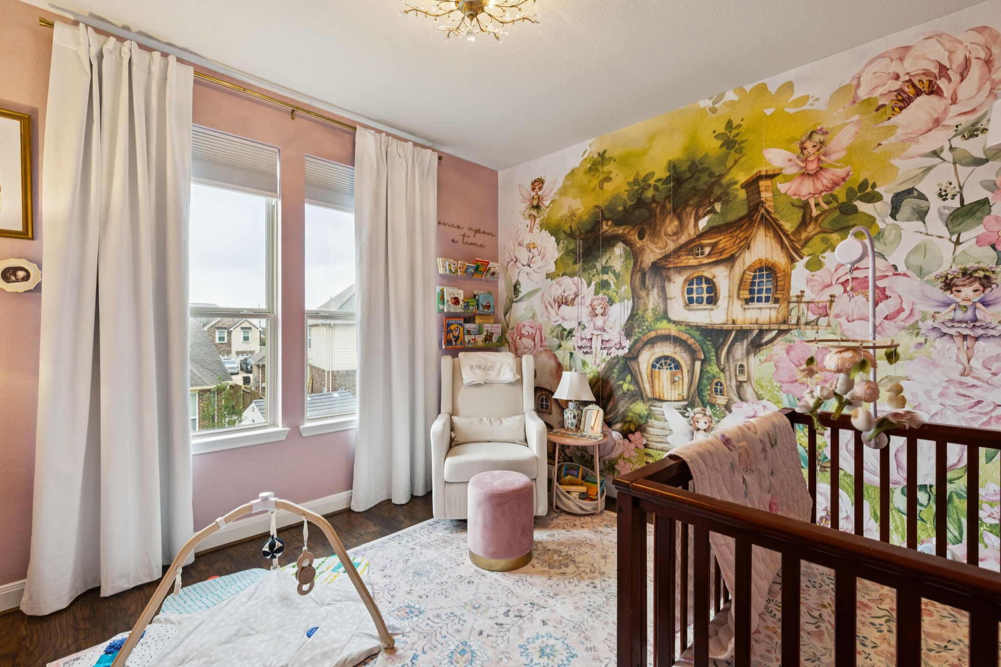 1118 Fragile Sail Court Katy, TX 77494 - Photo 22 of 36 In this enchanting nursery, storytelling comes to life with a floor-to-ceiling whimsical forest mural that creates a magical backdrop for play and rest. Large windows draped in soft white curtains fill the room with natural light, highlighting the rich wood look laminate flooring.