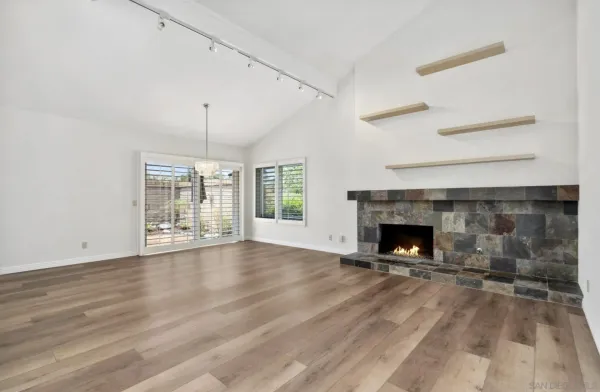 an empty room with wooden floor fireplace and windows