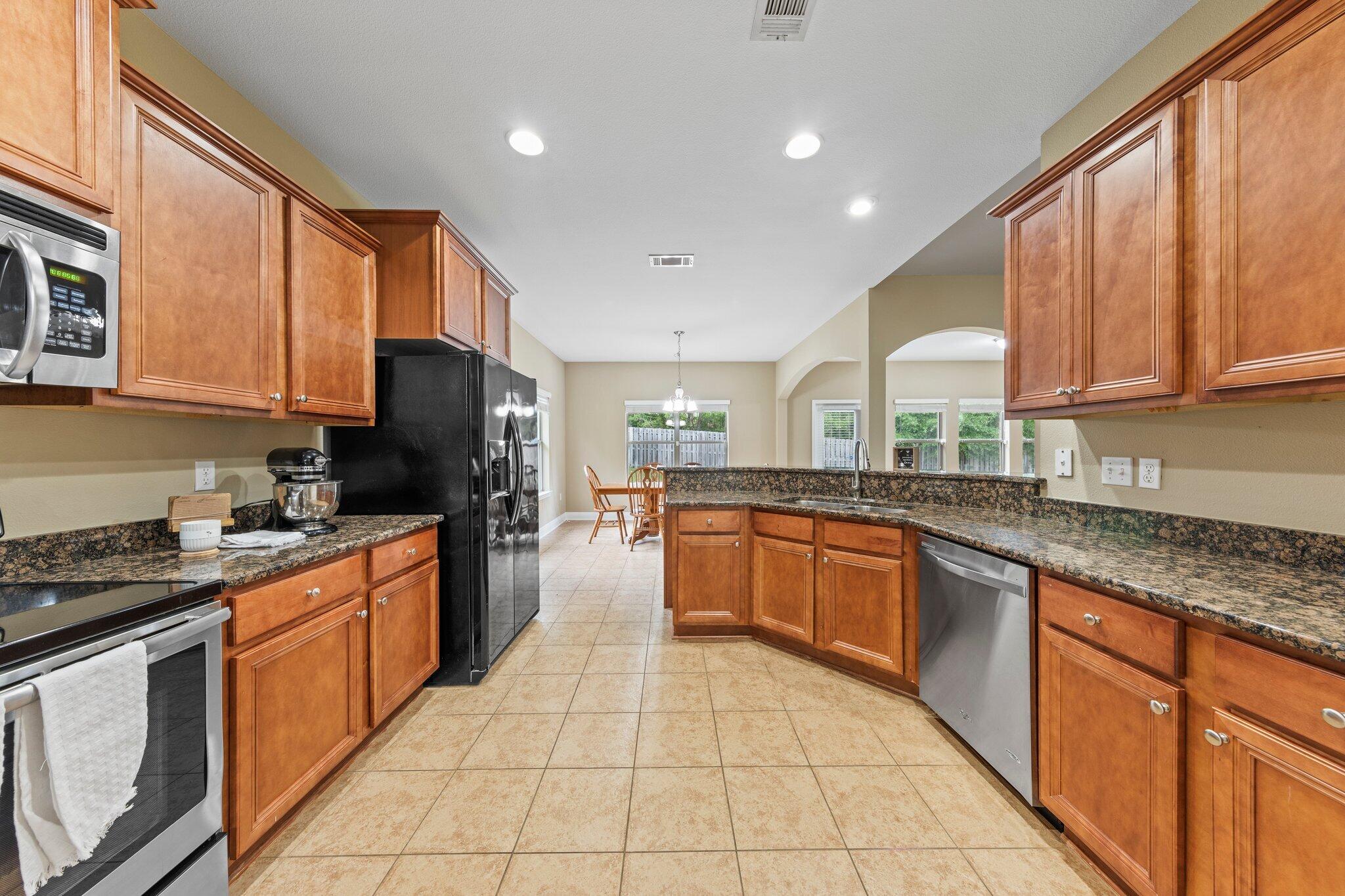 613 Red Fern Road Crestview, FL 32536 - Photo 26 of 39 a large kitchen with stainless steel appliances granite countertop a stove top oven a sink dishwasher a dining table and chairs with wooden cabinets