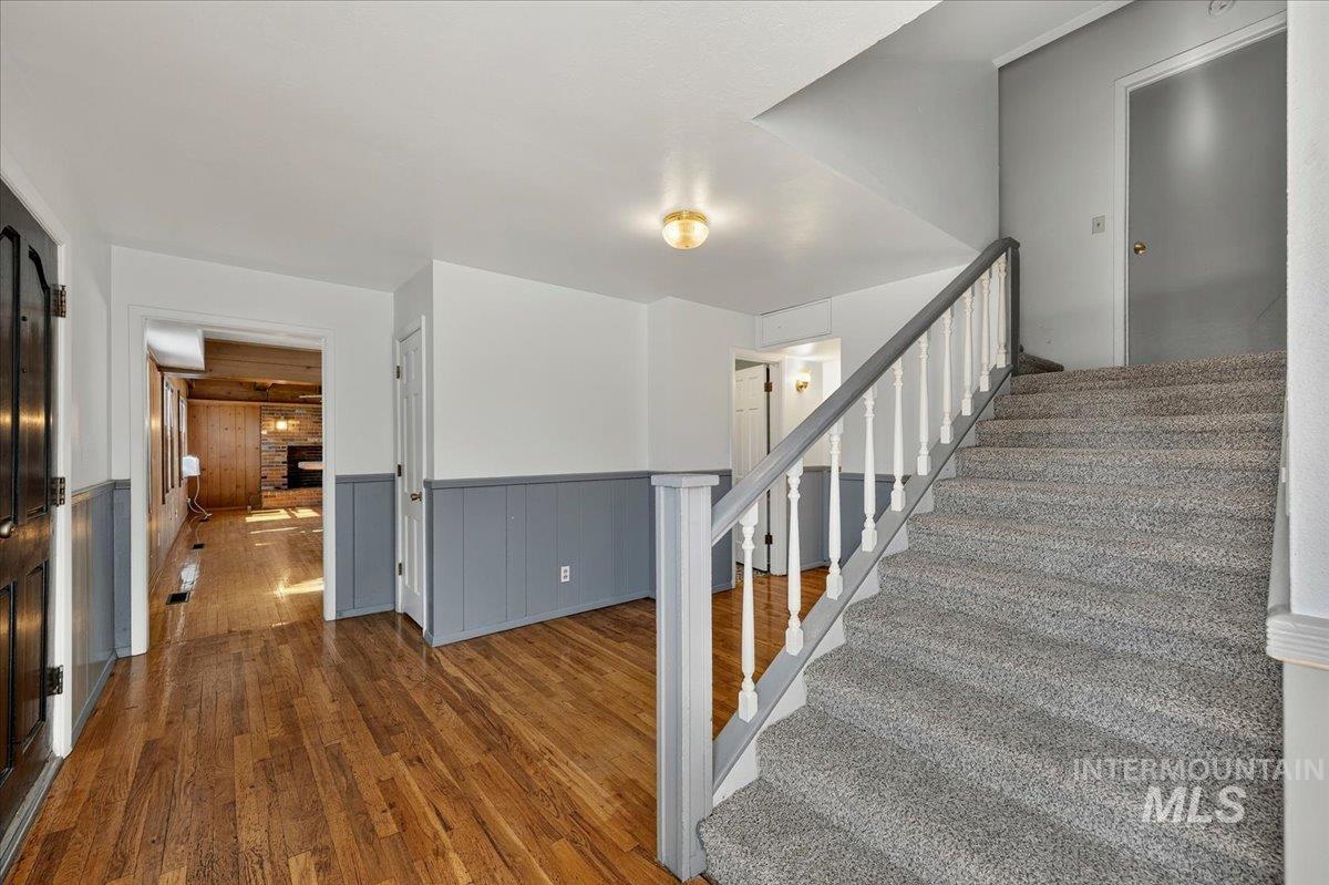 2160 South Five Mile Road Boise, ID 83709 - Photo 14 of 41 Entryway featuring wood-finish flooring, white walls with blue-grey wainscoting, and a carpeted staircase with a white and grey banister