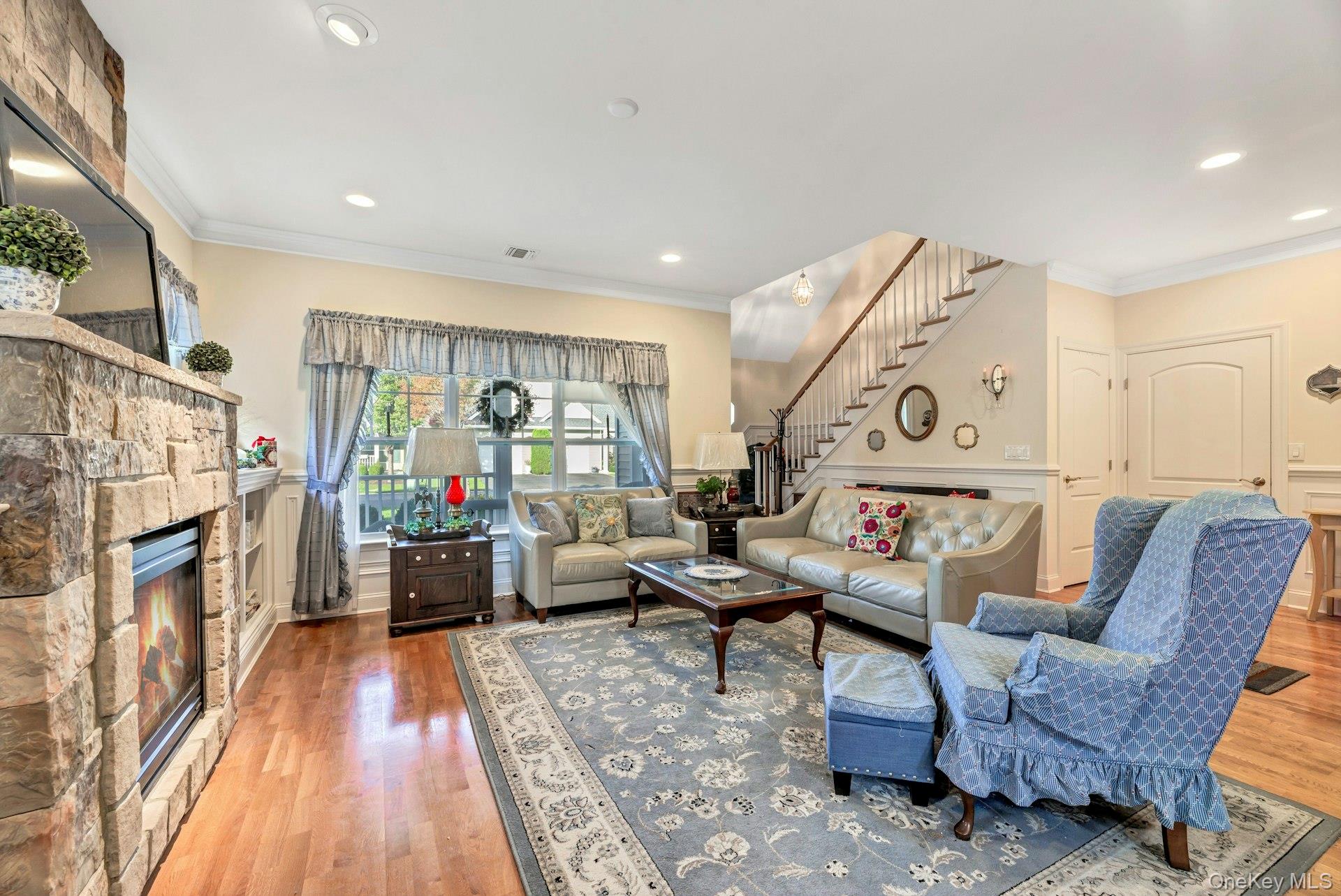 159 Stoneleigh Drive Riverhead, NY 11901 - Photo 9 of 24 Living area featuring crown molding, light wood-type flooring, wainscoting, a fireplace, and stairs