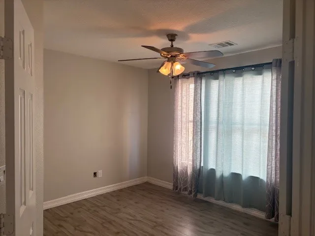 an empty room with wooden floor fan and windows