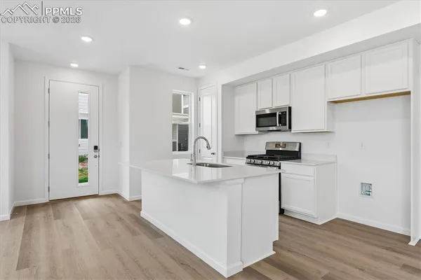 a kitchen with stainless steel appliances a stove a sink a refrigerator white cabinets and wooden floor