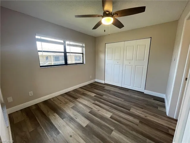an empty room with wooden floor chandelier fan and windows