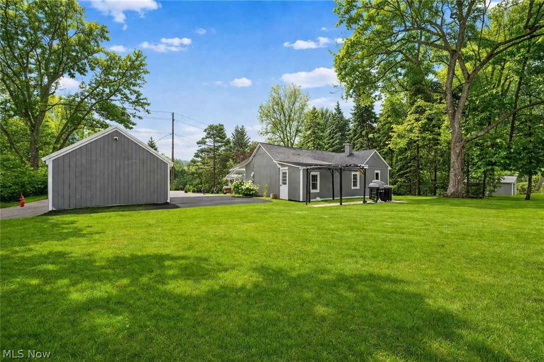 8564 Cedar Road Chesterland, OH 44026 - Photo 3 of 43 The property offers a vast lawn, a gray-sided residence with a pergola-covered patio, and a separate gray-sided outbuilding