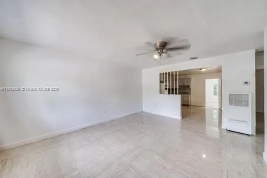 an empty room with a ceiling fan and kitchen view