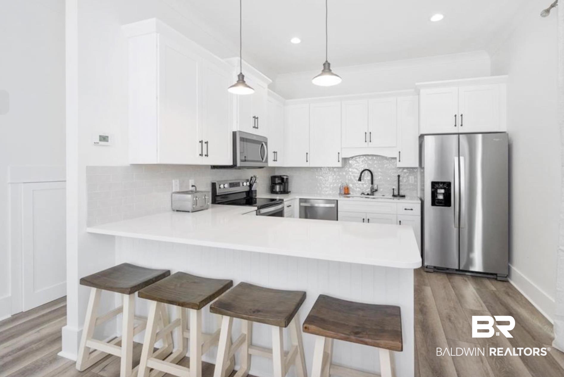 20 West Gate Orange Beach, AL 36561 - Photo 6 of 15 Kitchen with stainless steel appliances, a kitchen bar, white cabinetry, light wood-style flooring, and a peninsula