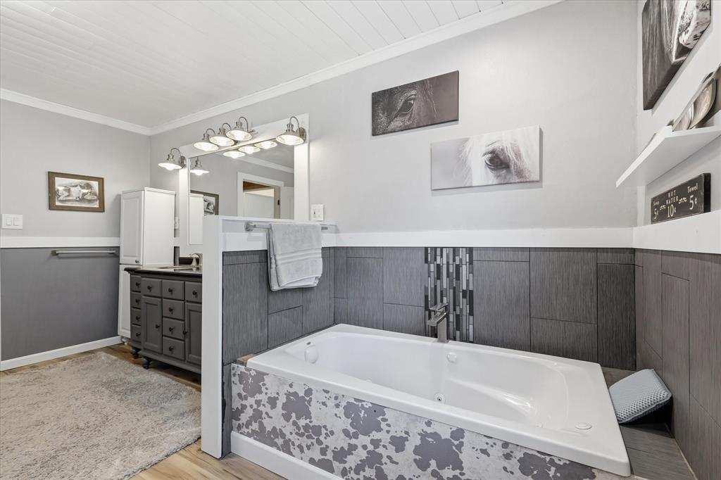 237 Brenda Lane Gainesville, TX 76240 - Photo 23 of 40 Bathroom featuring an inset bathtub with a tiled surround, a large vanity with a rectangular mirror, a paneled ceiling, and wood-finish flooring