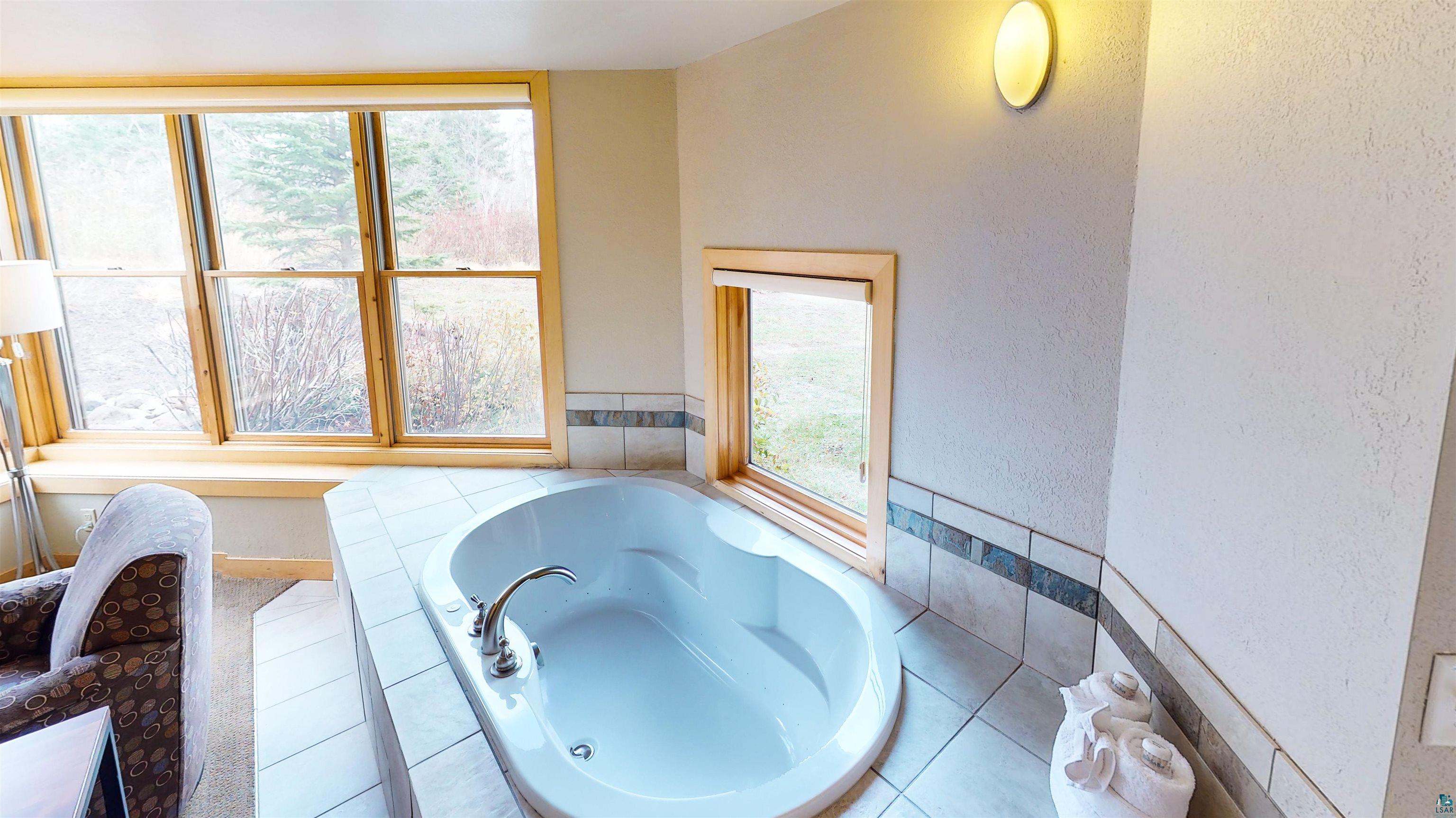 40 Surfside Drive, Unit 5D Tofte, MN 55615 - Photo 23 of 37 Built-in soaking tub with tiled surround, large windows with natural wood frames, and a wall-mounted light fixture